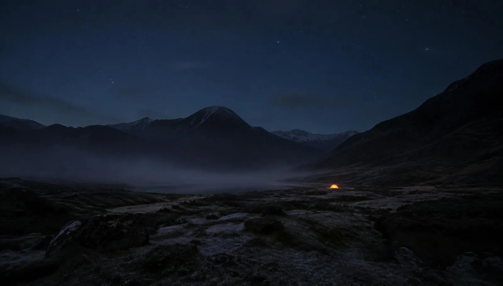 Cold British campsite at night with dark mountains and a single lit tent in the distance
